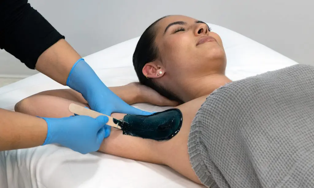 An image of someone receiving waxing for hair removal in her underarms