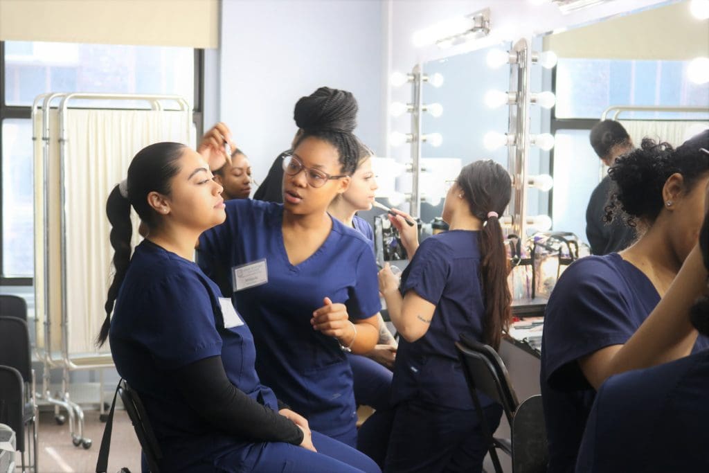 An Atelier Esthetique student providing makeup to another student, an example of the cross between cosmetology and esthetics.