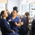 An Atelier Esthetique student providing makeup to another student, an example of the cross between cosmetology and esthetics.